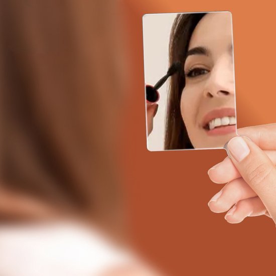 Vrouw die haar wimpers borstelt terwijl ze in een kleine handspiegel kijkt, bruine achtergrond