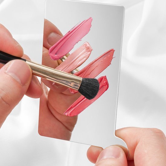 Hand houdt spiegel vast met lippenstiftstalen en penseel dat roze kleuren aanbrengt op spiegel oppervlak.