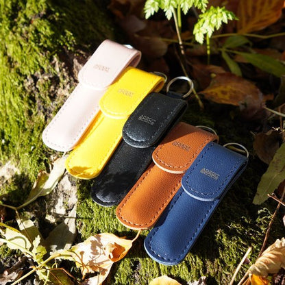 Vijf leren sleutelhangers in verschillende kleuren liggend op mos en herfstbladeren buiten