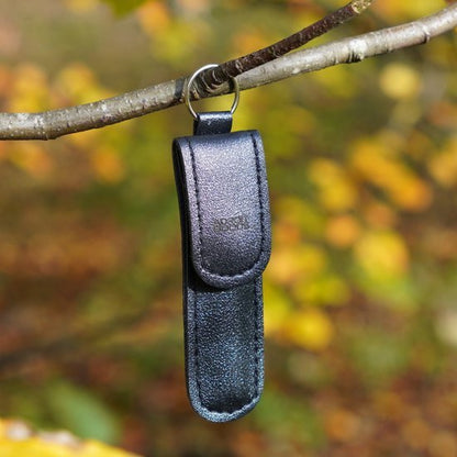 Zwarte leren sleutelhanger met metalen ring hangend aan een tak in de natuur
