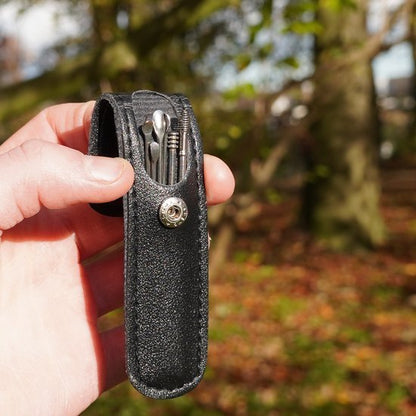 Hand houdt klein zwart leren hoesje met metalen gereedschap en click sluiting buitenzijde