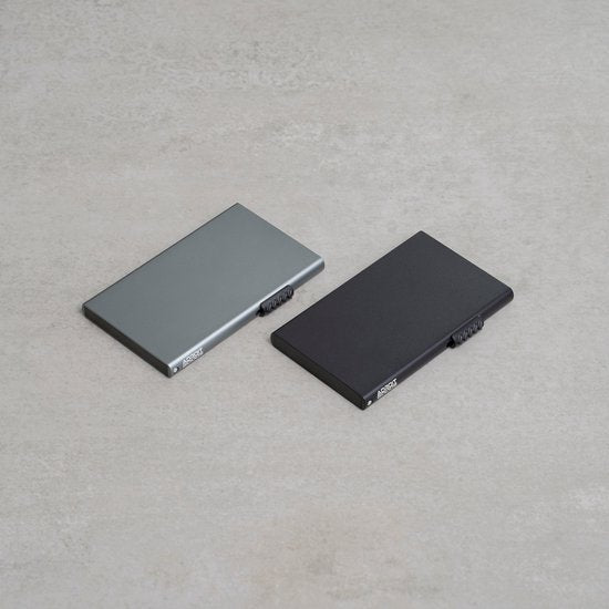 Twee platliggende, minimalistische metalen accessoires in grijs en zwart op een neutrale achtergrond.