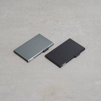 Twee platliggende, minimalistische metalen accessoires in grijs en zwart op een neutrale achtergrond.