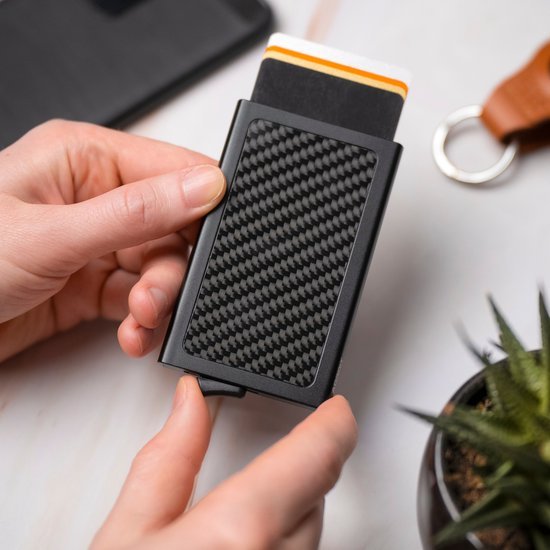 Hand die een slanke zwarte portemonnee met carbonprint en kaarten vasthoudt boven witte ondergrond