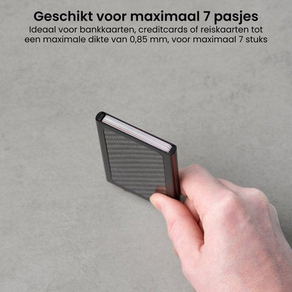 Hand die een compact zwart kaartetui met carbontextuur vasthoudt tegen een grijze achtergrond