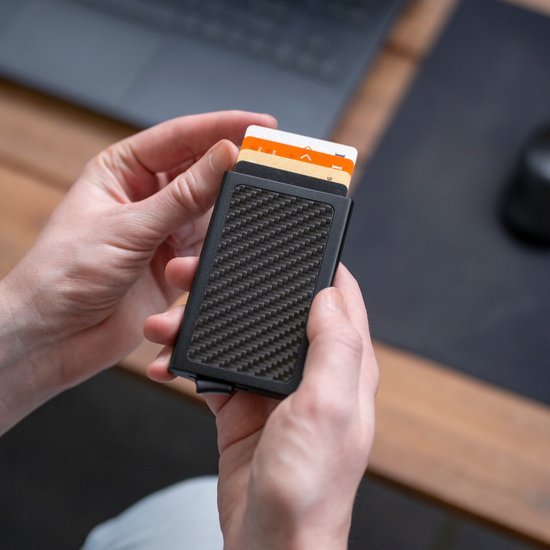 Handen houden een zwarte kaarthouder met een carbon fiber patroon en zichtbare kaarten vast