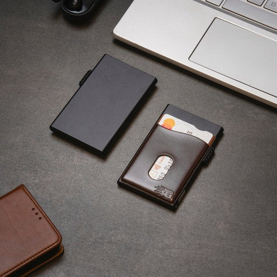 Minimalistisch zwart metalen kaarthouder en bruin lederen portemonnee op grijze tafel naast laptop