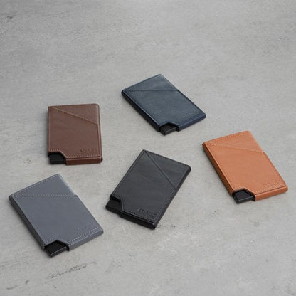 Vijf slanke leren portefeuilles in diverse kleuren op een grijze achtergrond gelegd.