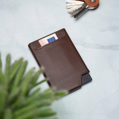 Bruine leren portemonnee met een bankbiljet en sleutels op een lichte ondergrond naast een plant