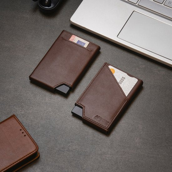 Twee stijlvolle bruine leren kaarthouders naast een laptop op een donker bureau gelegen.