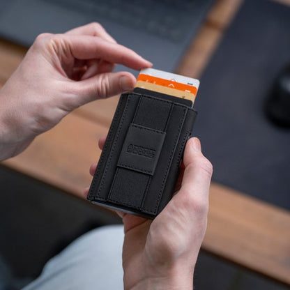 Hand houdt zwarte leren portemonnee met kaartjes tegen vervaagde houten achtergrond.