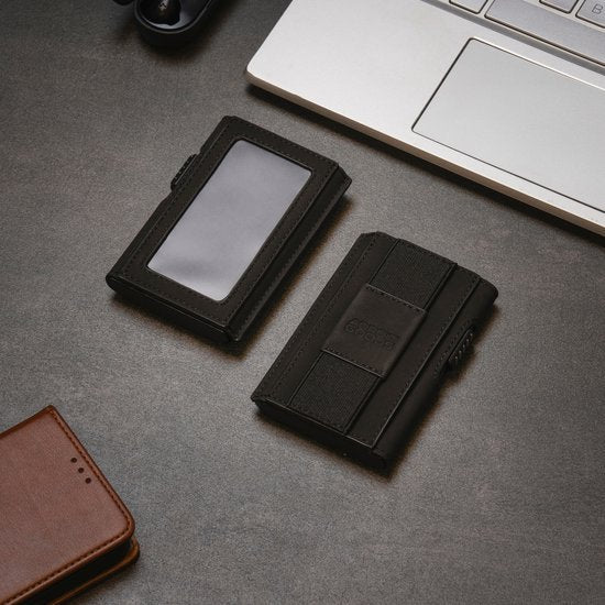 Twee zwarte leren portemonnees liggen naast een laptop op een grijze tafelblad.