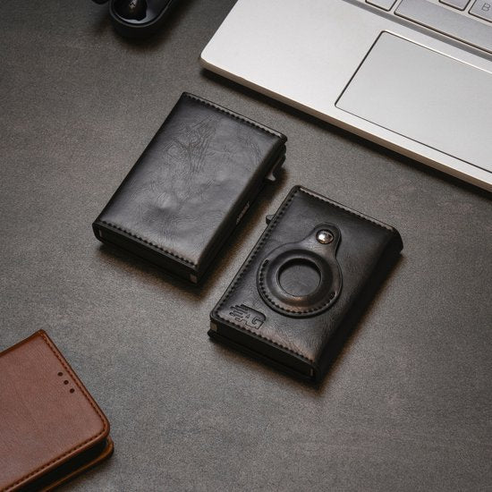 Twee zwarte leren portemonnees op een grijs oppervlak naast een laptop en een bruine leren portemonnee