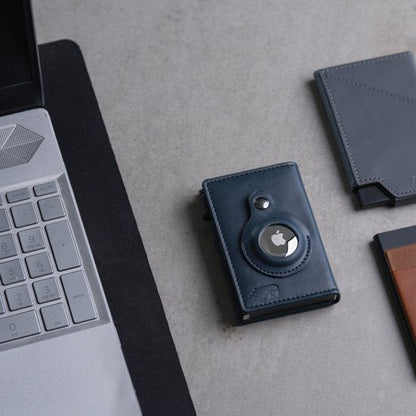 Laptop naast leren kaarthouders met een ronde metalen accessoire op grijze ondergrond