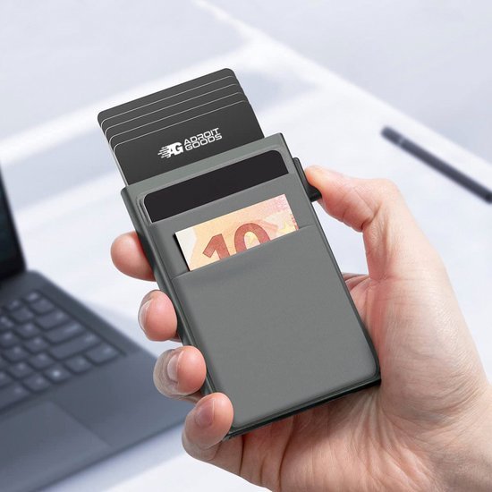 Hand houdt compacte zwarte portemonnee met pasjes en biljetten, naast laptop zichtbaar.