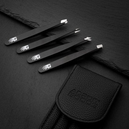 Vier zwarte pincetten met verschillende punten en een zwart leren etui op donkere ondergrond