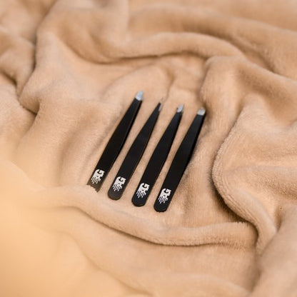 Vier zwarte pincetten met verschillende uiteinden op een zachte beige stof gelegd