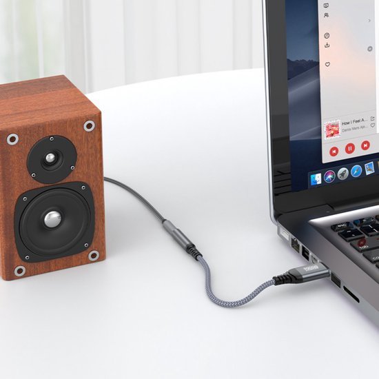 Houten luidspreker aangesloten op laptop via een grijze audiokabel op een witte tafel