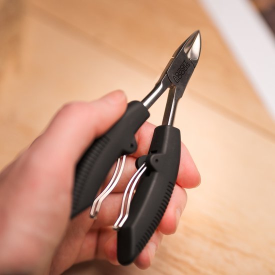 Hand die zwarte kniptang met metalen snijblad vasthoudt op houten achtergrond close-up