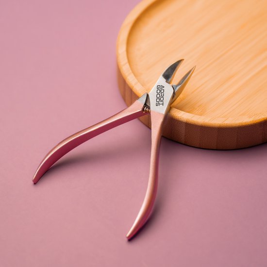 roze metalen nagelknipper met scherpe punten op ronde houten plank tegen roze achtergrond