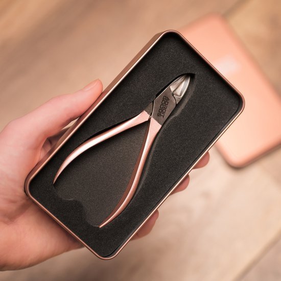 Hand houdt roségouden nagelknipper in zwart kussentje binnen metalen doosje