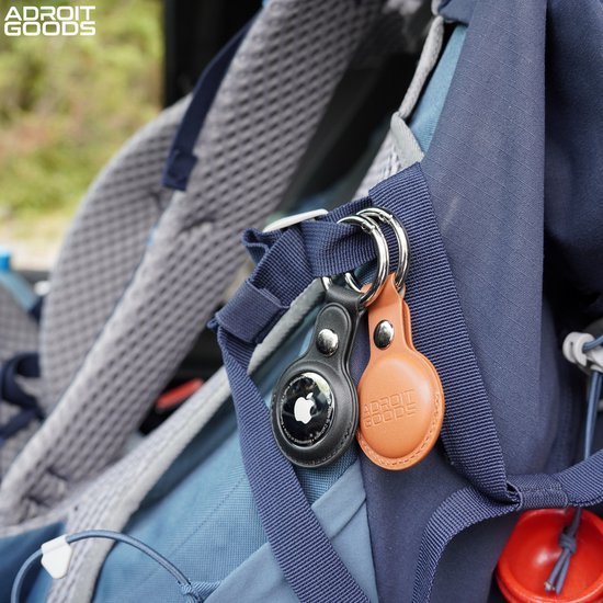 Twee leren sleutelhouders met metalen ring aan een blauwe rugzak bevestigd dichtbij een sportieve stoel
