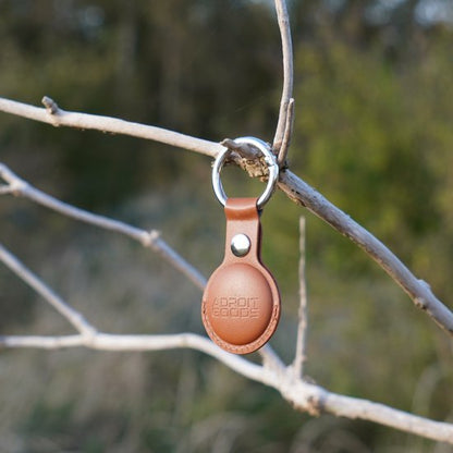 Bruine leren sleutelhanger met metalen ring, hangend aan een tak in de natuur.