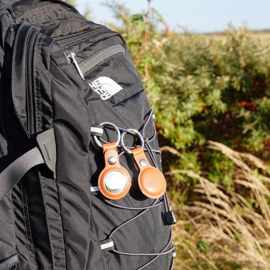 Zwarte rugzak met twee leren sleutelhangers en groen struikgewas op de achtergrond