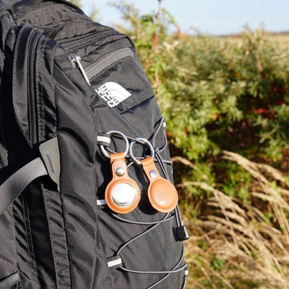 Zwarte rugzak met twee leren sleutelhangers en groen struikgewas op de achtergrond