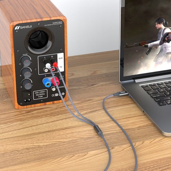 Aansluiting van een houten speaker met kabels op een laptop die een actiegame toont.