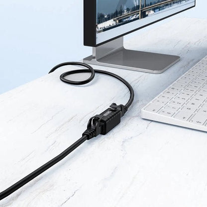 Zwarte kabel met connector aangesloten op een moderne monitor op een witte marmeren tafel
