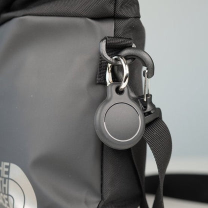 Zwarte sleutelhanger met ronde hanger bevestigd aan zwarte tas met karabijnhaak