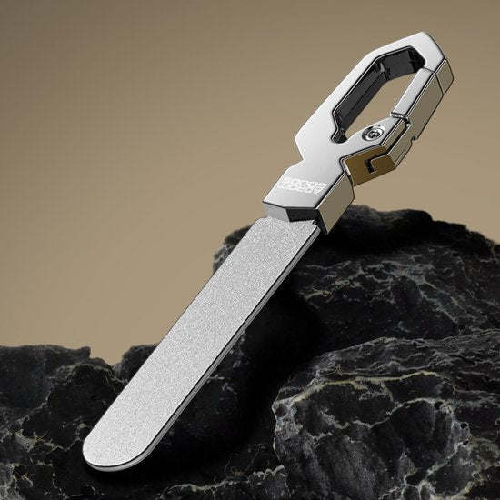 Stijlvolle zilverkleurige sleutelhanger met geïntegreerde nagelvijl op zwarte rotsen.