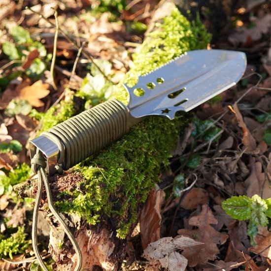 Tuinschepje met metalen blad en handvat gewikkeld in groen touw, rustend op mos en bladeren