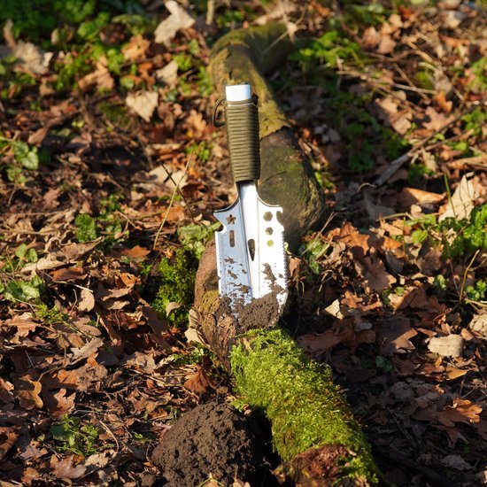 Metalen tuingereedschap met groen handvat steekt in mos bedekt hout in bosrijke omgeving.
