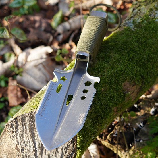 Stevige multitool schop met groen handvat op mosbedekt stuk hout buiten in natuur