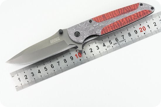 Opvouwbaar zakmes met roestvrijstalen lemmet en handgreep met rood patroon naast liniaal