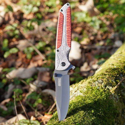 Opengeslagen mes met bruine handgreep en gegraveerd metalen frame op mosbedekt hout.