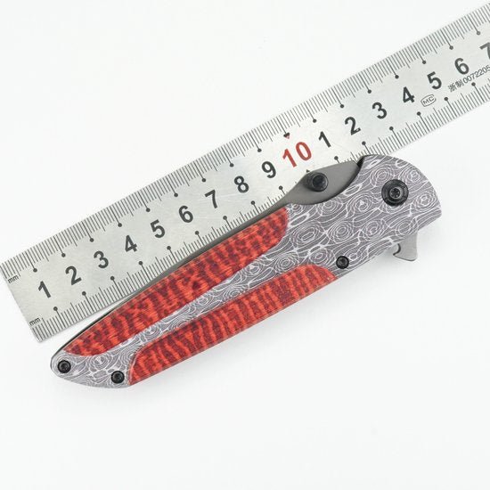 Opgevouwen zakmes met rood patroon en zilverkleurig handvat naast metalen liniaal.