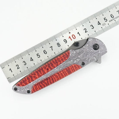 Opgevouwen zakmes met rood patroon en zilverkleurig handvat naast metalen liniaal.