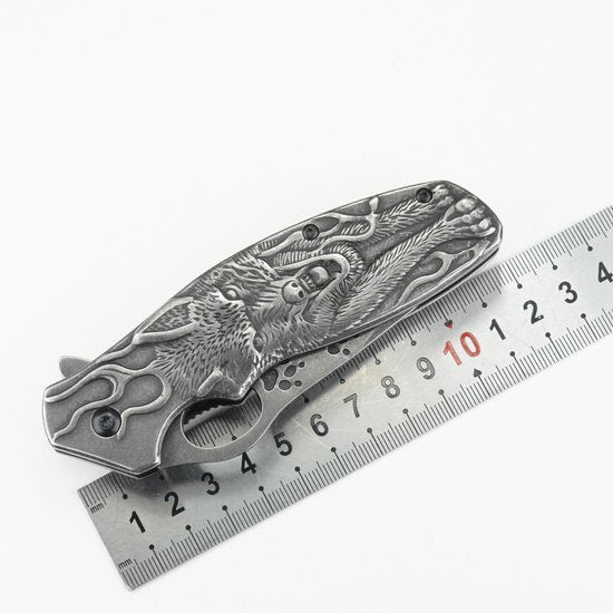 Gesloten mes met gedetailleerd drakenmotief op metalen handgreep naast liniaal