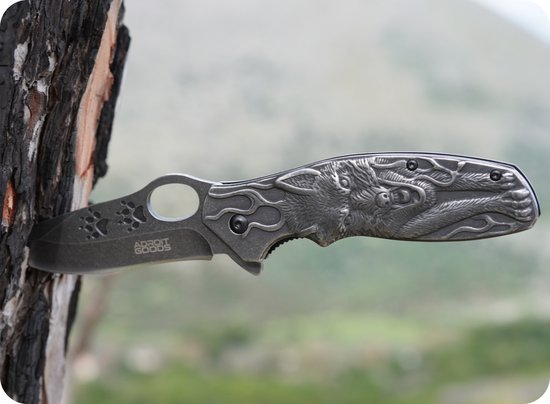 Vouwmes met gedetailleerde wolfgravure in roestvrijstalen handgreep tegen boomstam