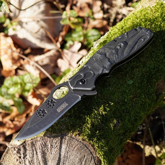 Vouwmes met zwarte gegraveerde handgreep en lemmet op mos bedekte boomstam geplaatst.