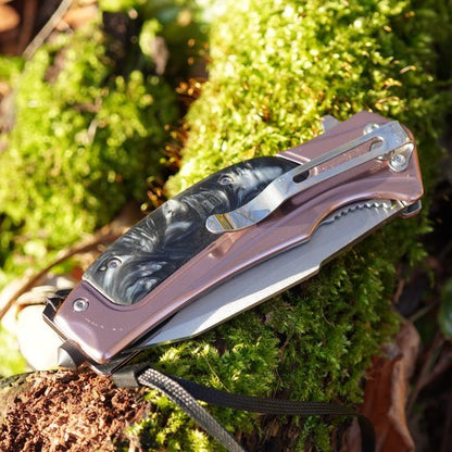 Opvouwbaar mes met decoratief handvat en clip, rustend op mosbedekt hout.