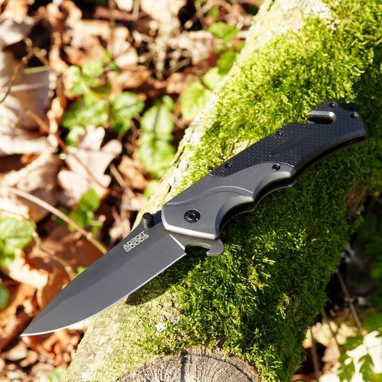 zwarte inklapbaar mes met textuurhendel liggend op met mos bedekt boomstam