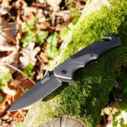 zwarte inklapbaar mes met textuurhendel liggend op met mos bedekt boomstam