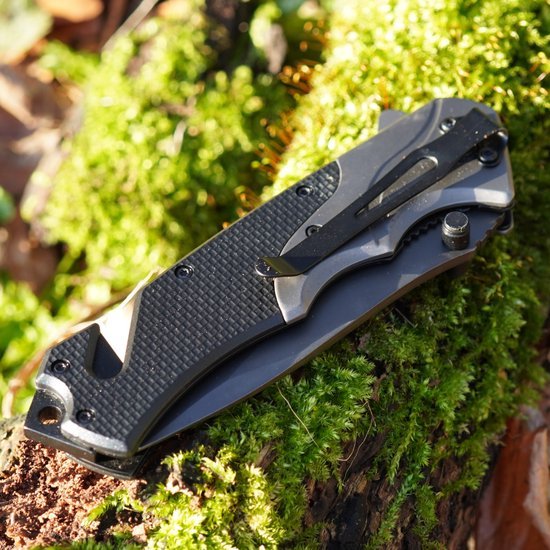 Gesloten zakmes met zwart handvat en metalen clip op groen mos en hout geplaatst