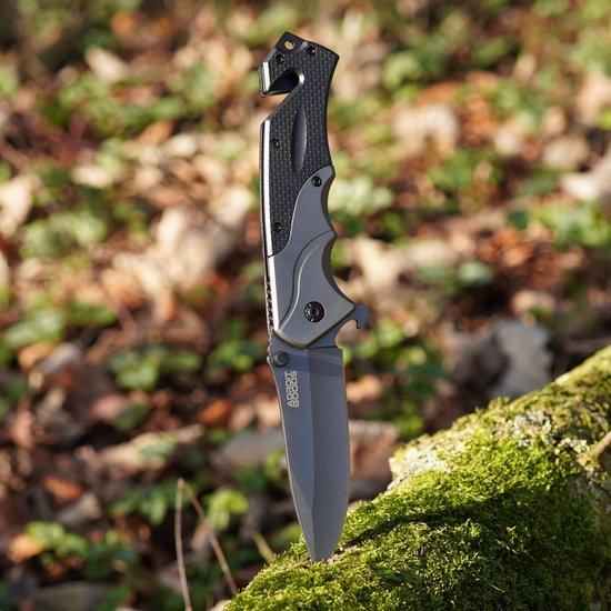 Vouwmes met zwart handvat en grijs lemmet, geplaatst in mosrijke houten ondergrond buiten