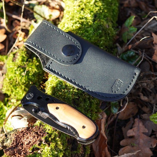 Opgevouwen zakmes met houten handvat naast zwarte leren hoes op mos en bladeren