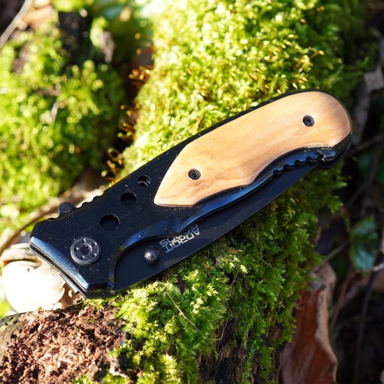 Opgevouwen zakmes met houten handvat op mos bedekt bosgrond in natuurlijk licht